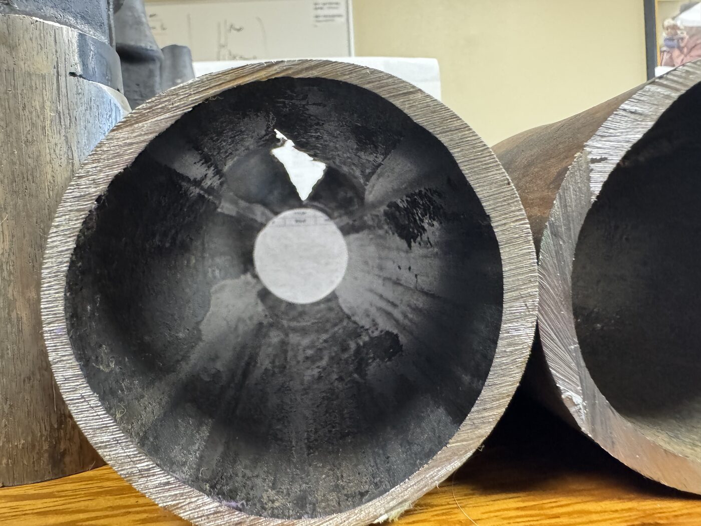 Photo: the cut end of a thick steel oil-well tubing joint, its inner bore polished and worn, with a hole worn clean through the wall where the rod scraped through; a second tubing section sits beside it.